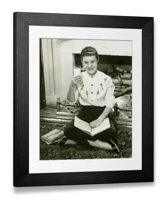 Framed Print : Young woman sitting by fireplace, holding glass of milk in raised hand, (B&W), portrait Framed Print : Young woman sitting by fireplace, holding glass of milk in raised hand, (B&W), portrait