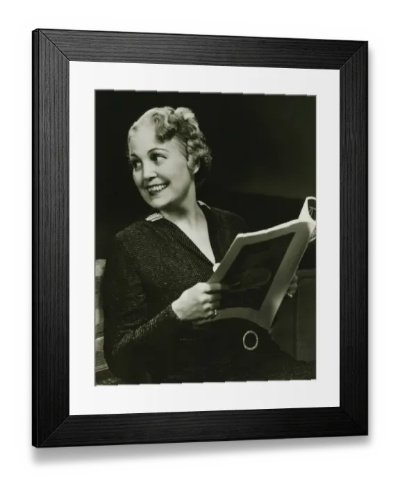 Framed Print : Well groomed mature woman holding fashion magazine in living room, (B&W), portrait