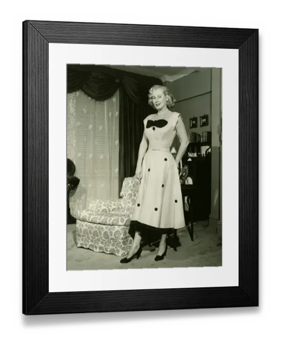 Framed Print : Woman in fashionable dress standing by armchair in living room, (B&W), portrait Framed Print : Woman in fashionable dress standing by armchair in living room, (B&W), portrait