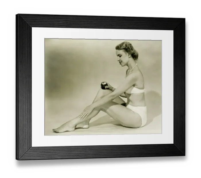 Framed Print : Young woman in bikini sitting, putting cream on leg, (B&W) Framed Print : Young woman in bikini sitting, putting cream on leg, (B&W)