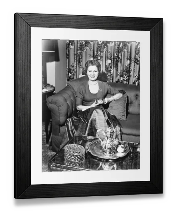 Framed Print : Woman sitting in rich living room, holding cup of coffee, (B&W) Framed Print : Woman sitting in rich living room, holding cup of coffee, (B&W)