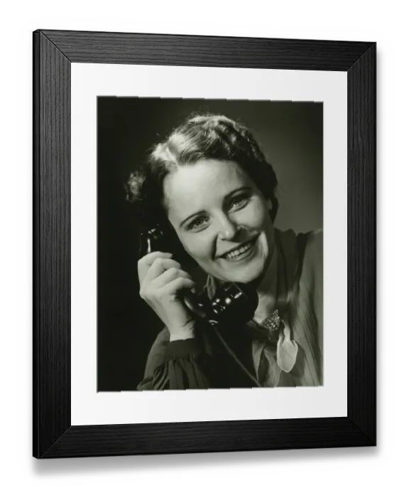 Framed Print : Smiling woman on phone posing in studio, (B&W), close-up, portrait Framed Print : Smiling woman on phone posing in studio, (B&W), close-up, portrait