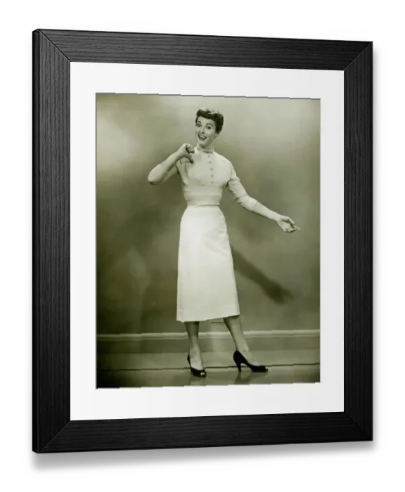 Framed Print : Woman in white dress pointing to herself in studio, (B&W), portrait Framed Print : Woman in white dress pointing to herself in studio, (B&W), portrait