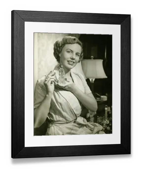 Framed Print : Young woman putting on perfume, at home, (B&W), portrait