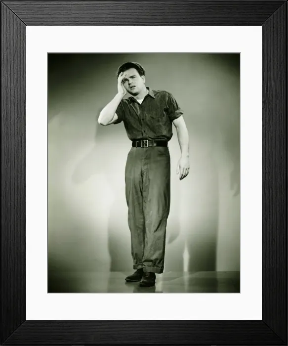 Framed Print : Young man standing in studio, holding hand on forehead, (B&W) Framed Print : Young man standing in studio, holding hand on forehead, (B&W)