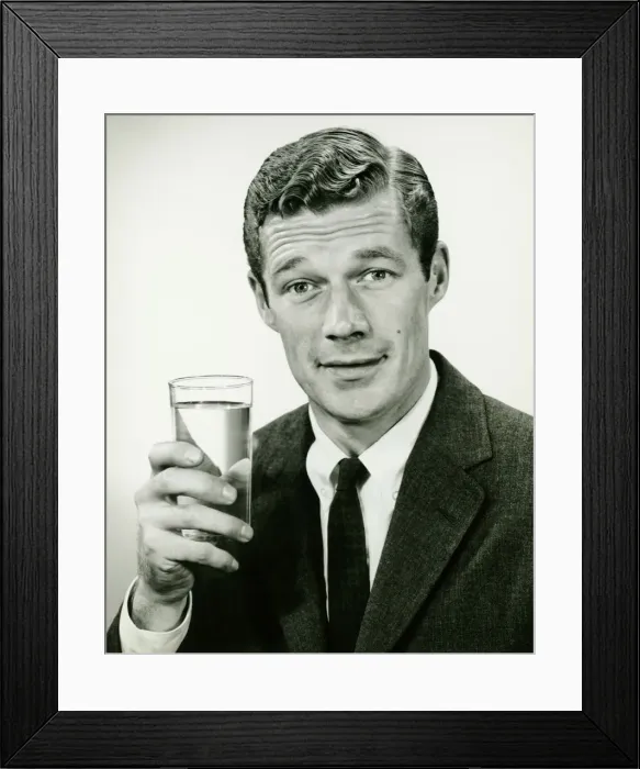 Framed Print : Young businessman holding glass of water, posing in studio, (B&W), portrait