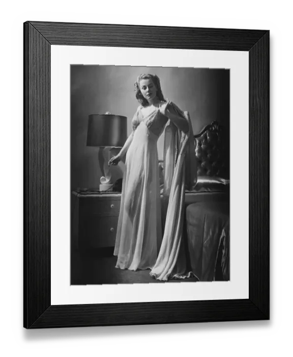 Framed Print : Young woman standing by bed wearing dressing gown, (B&W)