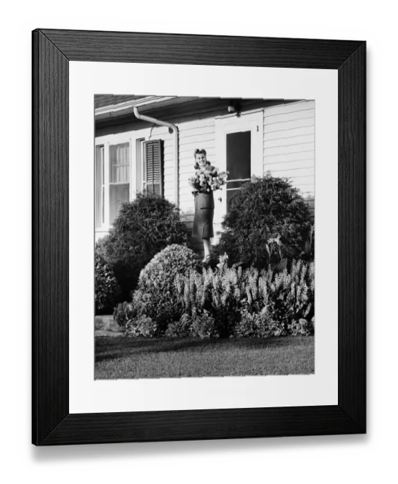 Framed Print : Woman standing on front porch of house holding bunch of flowers, (B&W) Framed Print : Woman standing on front porch of house holding bunch of flowers, (B&W)