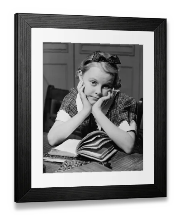 Framed Print : Bored young girl (12-13) at table with book, (B&W) Framed Print : Bored young girl (12-13) at table with book, (B&W)