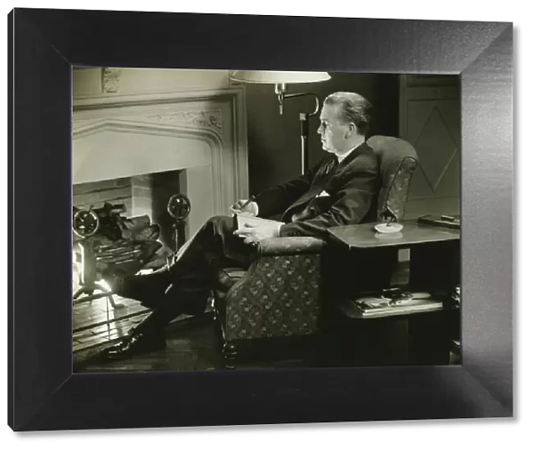 Man sitting on armchair in front of fireplace, (B&W)