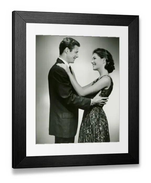 Framed Print : Young couple standing face to face, smiling, in studio, (B&W)
