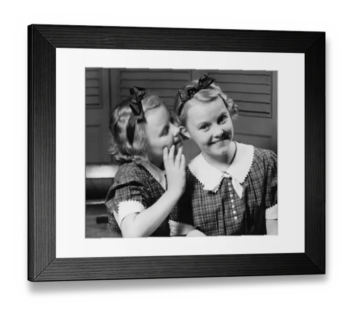 Framed Print : Girl (12-13) indoors whispering into ear of twin sister, (B&W) Framed Print : Girl (12-13) indoors whispering into ear of twin sister, (B&W)