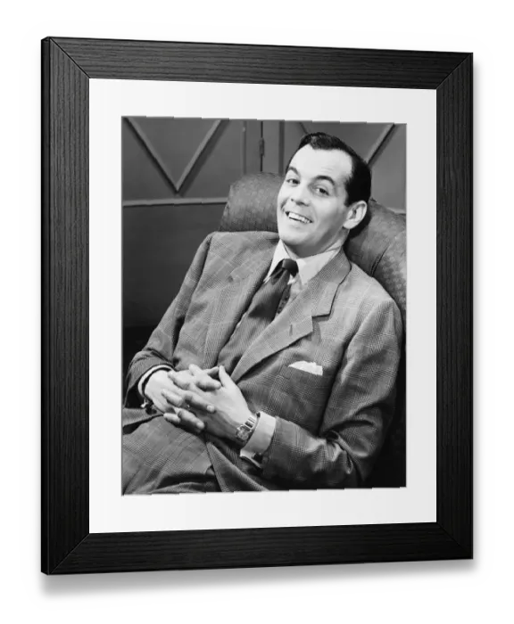 Framed Print : Smiling man in full suit reclining on chair, (B&W), portrait Framed Print : Smiling man in full suit reclining on chair, (B&W), portrait
