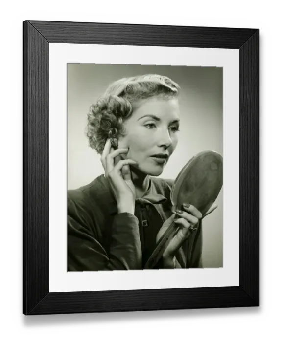Framed Print : Woman adjusting earring, holding hand mirror, (B&W), portrait Framed Print : Woman adjusting earring, holding hand mirror, (B&W), portrait
