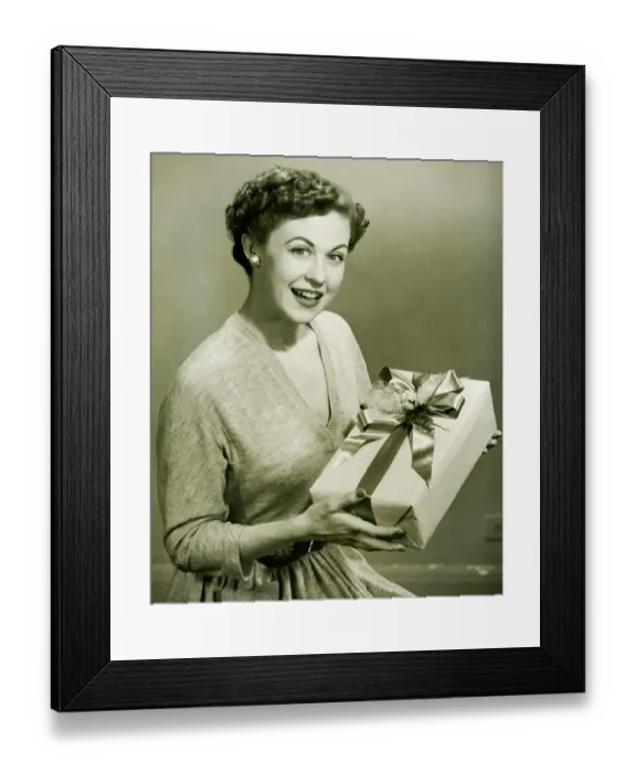 Framed Print : Woman holding wrapped gift in studio, (B&W), portrait Framed Print : Woman holding wrapped gift in studio, (B&W), portrait