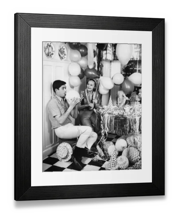 Framed Print : Couple blowing up balloons in kitchen for party, (B&W) Framed Print : Couple blowing up balloons in kitchen for party, (B&W)
