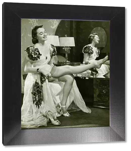 Glamorous woman in evening gown putting on silk stockings, (B&W)
