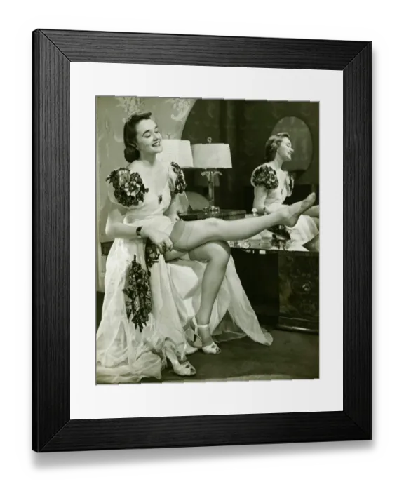 Framed Print : Glamorous woman in evening gown putting on silk stockings, (B&W) Framed Print : Glamorous woman in evening gown putting on silk stockings, (B&W)