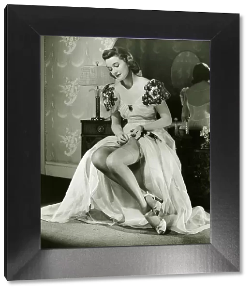 Glamorous woman in evening gown adjusting stockings, portrait, (B&W)