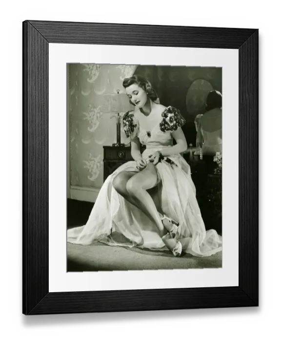 Framed Print : Glamorous woman in evening gown adjusting stockings, portrait, (B&W)