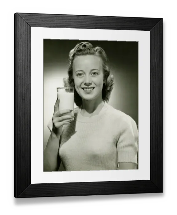 Framed Print : Smiling woman holding glass of milk in studio, (B&W), portrait Framed Print : Smiling woman holding glass of milk in studio, (B&W), portrait