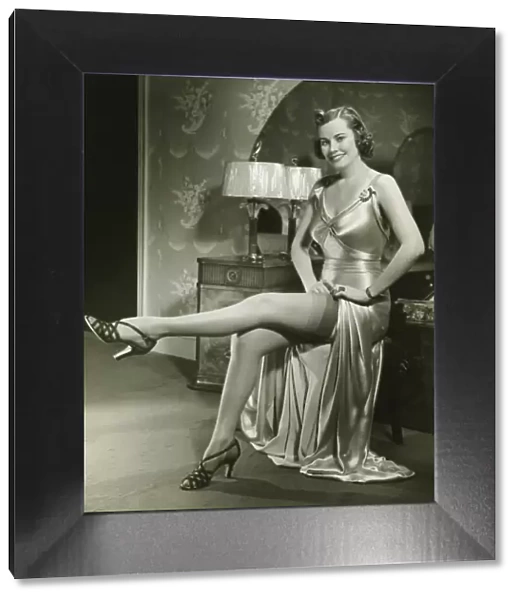 Woman in silk evening gown sitting by vanity table, showing leg, (B&W)