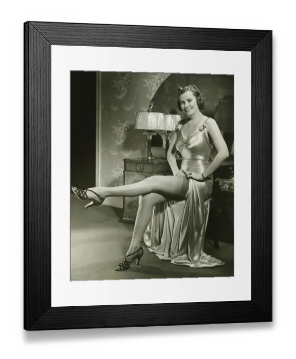 Framed Print : Woman in silk evening gown sitting by vanity table, showing leg, (B&W) Framed Print : Woman in silk evening gown sitting by vanity table, showing leg, (B&W)