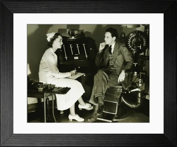 Framed Print : Nurse talking to patient in opticians examination room, (B&W) Framed Print : Nurse talking to patient in opticians examination room, (B&W)
