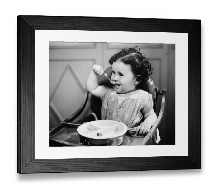 Framed Print : Baby girl (12-18 months) in highchair eating, (B&W) Framed Print : Baby girl (12-18 months) in highchair eating, (B&W)