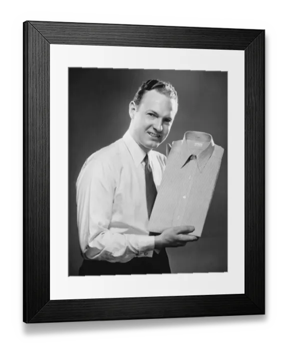 Framed Print : Man presenting folded shirt in studio, (B&W), portrait