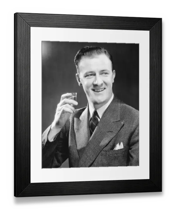 Framed Print : Smiling man holding up short glass with drink, (B&W), close-up Framed Print : Smiling man holding up short glass with drink, (B&W), close-up