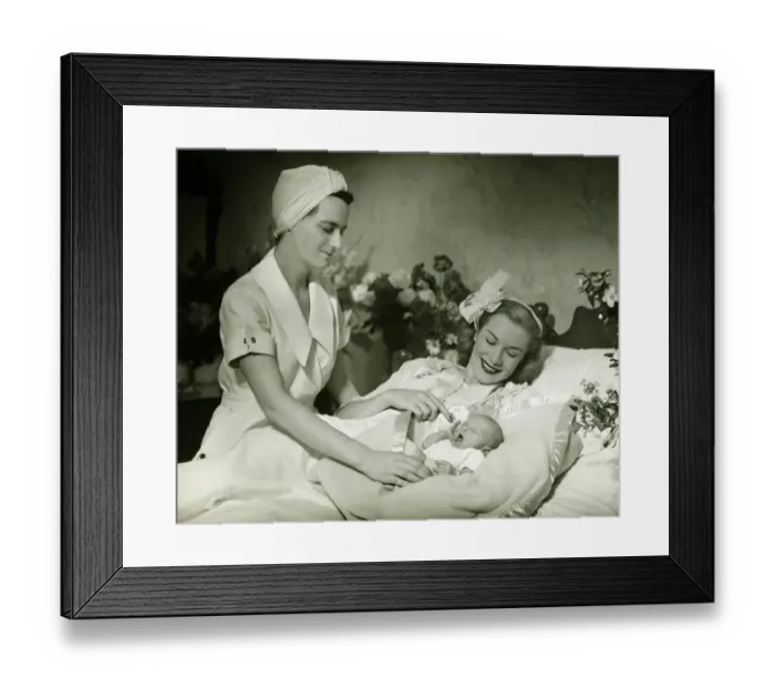 Framed Print : Mother lying in bed smiling to baby-child (0-6 months), nurse standing beside, (B&W)