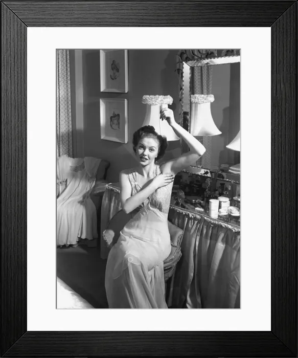 Framed Print : Woman sitting at vanity table, applying cosmetics, (B&W) Framed Print : Woman sitting at vanity table, applying cosmetics, (B&W)