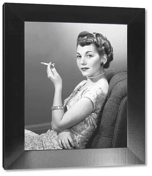 Elegant woman smoking cigarette in studio, (B&W), portrait
