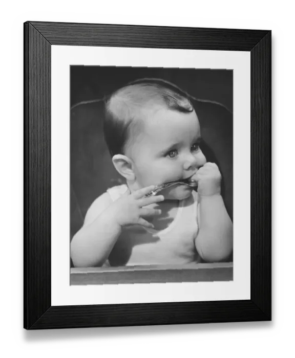 Framed Print : Baby boy (6-9 months) sitting in highchair, biting spoon (B&W) Framed Print : Baby boy (6-9 months) sitting in highchair, biting spoon (B&W)