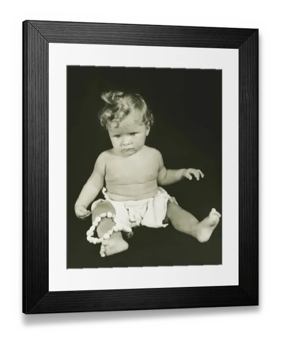 Framed Print : Baby girl (6-12 months) sitting against black background, (B&W), close-up Framed Print : Baby girl (6-12 months) sitting against black background, (B&W), close-up