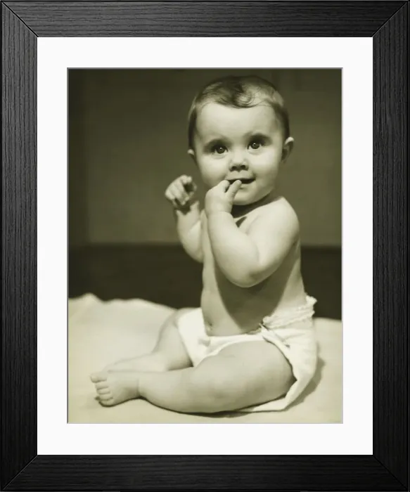 Framed Print : Baby boy (12-18 months) sitting on bedspread, sucking finger, (B&W), close-up