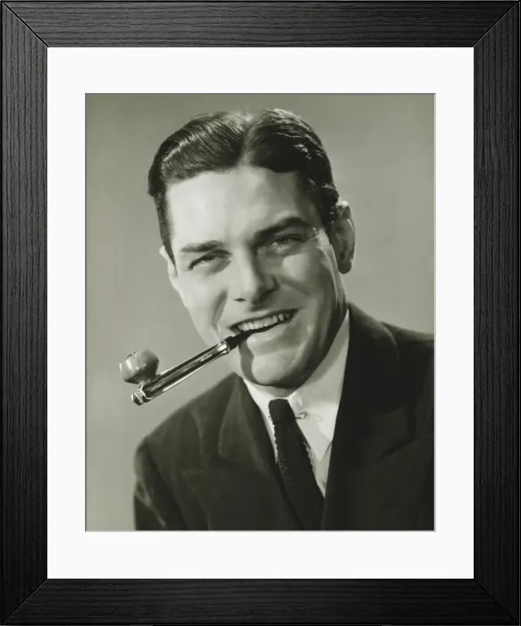 Framed Print : Young businessman in studio holding pipe in teeth, smiling, (B&W), portrait Framed Print : Young businessman in studio holding pipe in teeth, smiling, (B&W), portrait