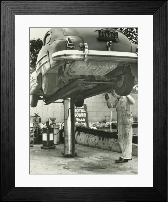 Framed Print : Man repairing uplifted car, (B&W), low section Framed Print : Man repairing uplifted car, (B&W), low section