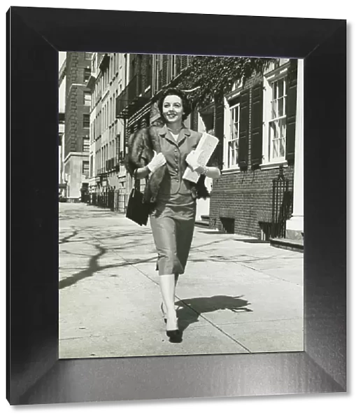 Elegant woman walking on sidewalk, holding bags, (B&W)