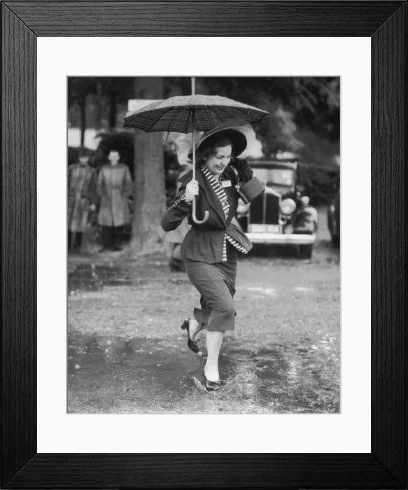Framed Print : Wet Feet. Circa 1945, A smartly dressed woman with an umbrella splashes