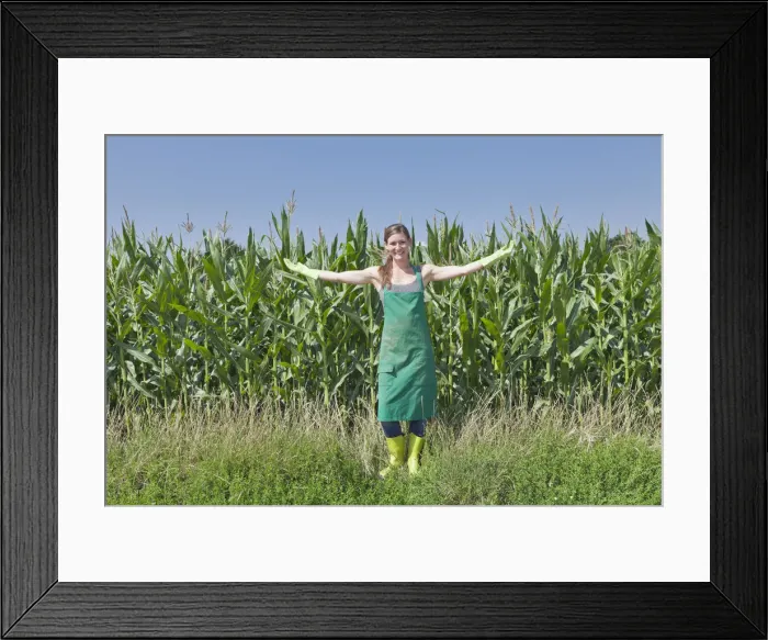 Framed Print : Young woman in work clothes standing with outstretched arms in front of a maize field, Baden-Wurttemberg, Germany Framed Print : Young woman in work clothes standing with outstretched arms in front of a maize field, Baden-Wurttemberg, Germany