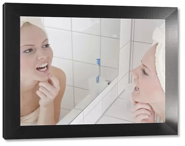 Woman with bath towel and towel on her head in front of the mirror in the bathroom