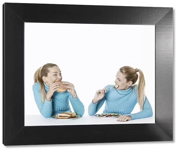 Two women eating food, one eating fast food, the other one eating uncooked vegetarian food