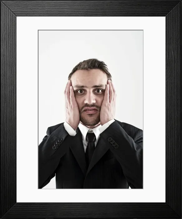 Framed Print : Desperate young man wearing a suit holding his hands to his face, worried Framed Print : Desperate young man wearing a suit holding his hands to his face, worried