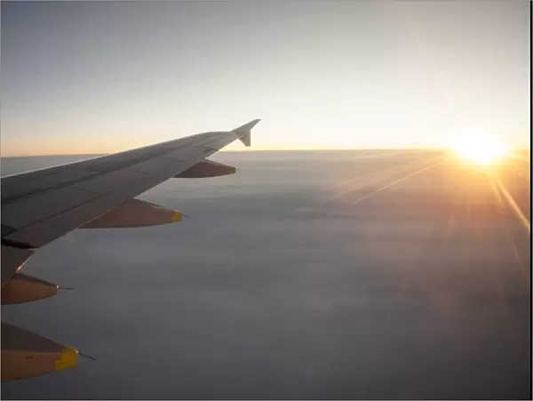 Sunrise from an airplane above the clouds with wing unit, above Norway