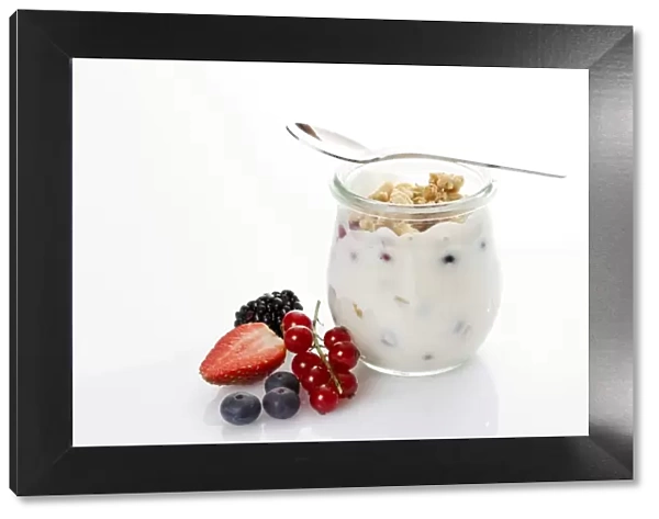Glass and spoon with muesli, yoghurt, berries, red currants, blueberries, strawberry, blackberry