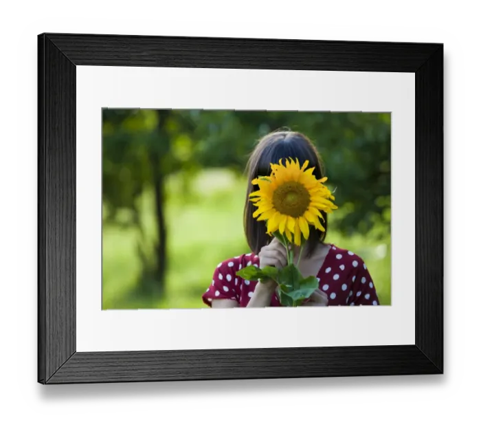 Framed Print : Young woman, 25, holding a sunflower in front of her face Framed Print : Young woman, 25, holding a sunflower in front of her face