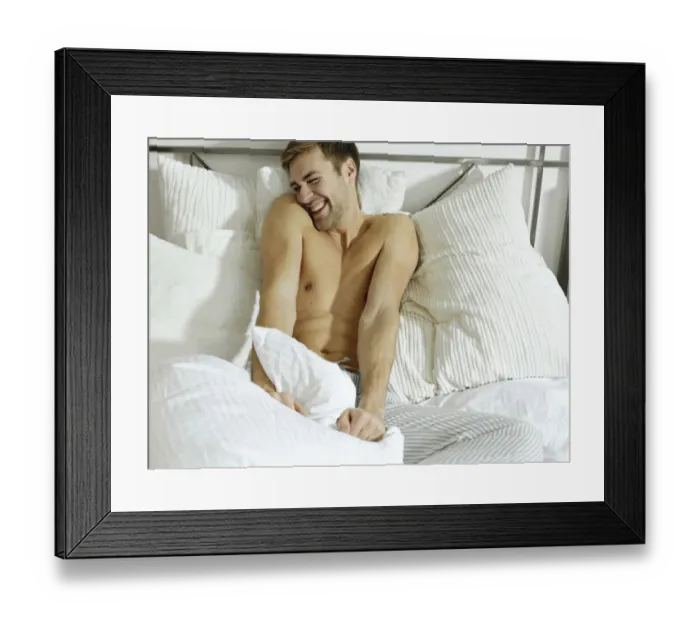 Framed Print : Charming bare chested man wearing pyjamas sitting on a bed, smiling