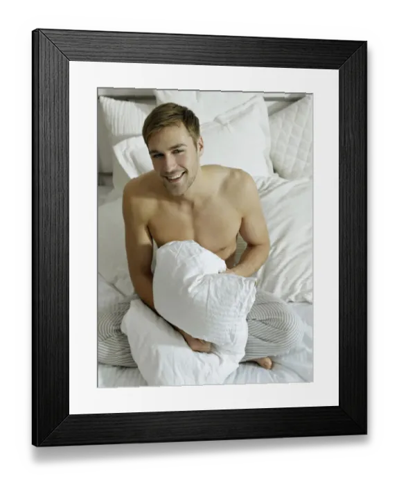 Framed Print : Charming bare chested man wearing pyjamas sitting on a bed, smiling Framed Print : Charming bare chested man wearing pyjamas sitting on a bed, smiling